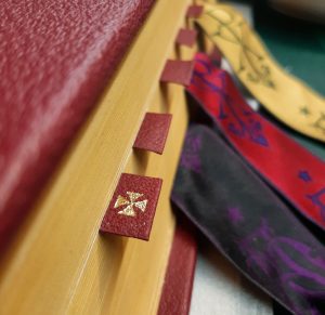 Gold cross on replacement leather page tab in a 1962 Missale Romanum with replacement Missal ribbons in the background