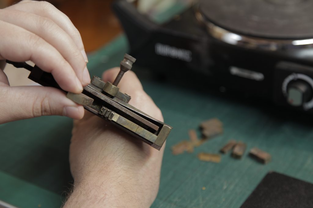 Bookbinder setting brass type in a handheld type holder