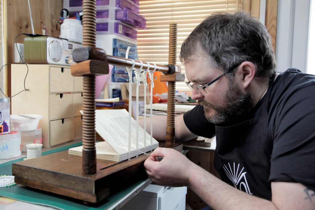 bookbinder resewing a book onto 4 tapes using a sewing frame