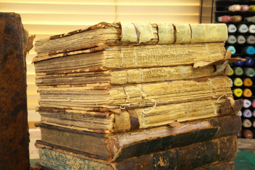 Stack of antique Jewish prayer books with missing spines and damaged pages