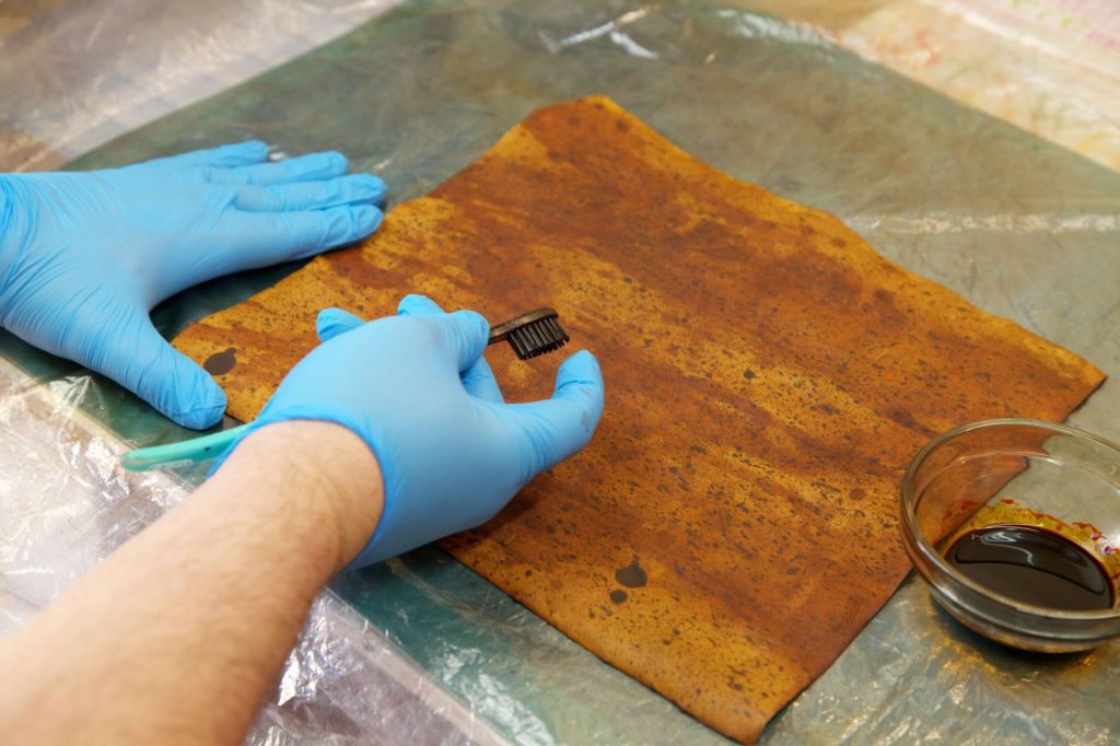Bookbinder wearing blue latex gloves sprinkling brown leather with black dye to recreate marbled leather pattern